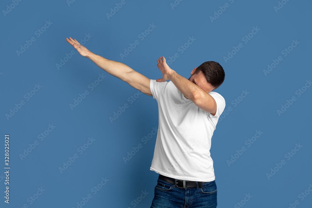 Winner's dabbing. Caucasian young man's portrait isolated on blue studio background. Beautiful male model in casual style, pastel colors. Concept of human emotions, facial expression, sales, ad. Winner's dabbing. Caucasian young man's portrait isolated on blue studio background. Beautiful male model in casual style, pastel colors. Concept of human emotions, facial expression, sales, ad.