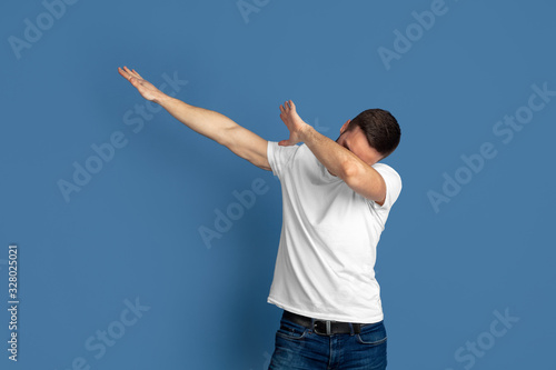 Winner's dabbing. Caucasian young man's portrait isolated on blue studio background. Beautiful male model in casual style, pastel colors. Concept of human emotions, facial expression, sales, ad.