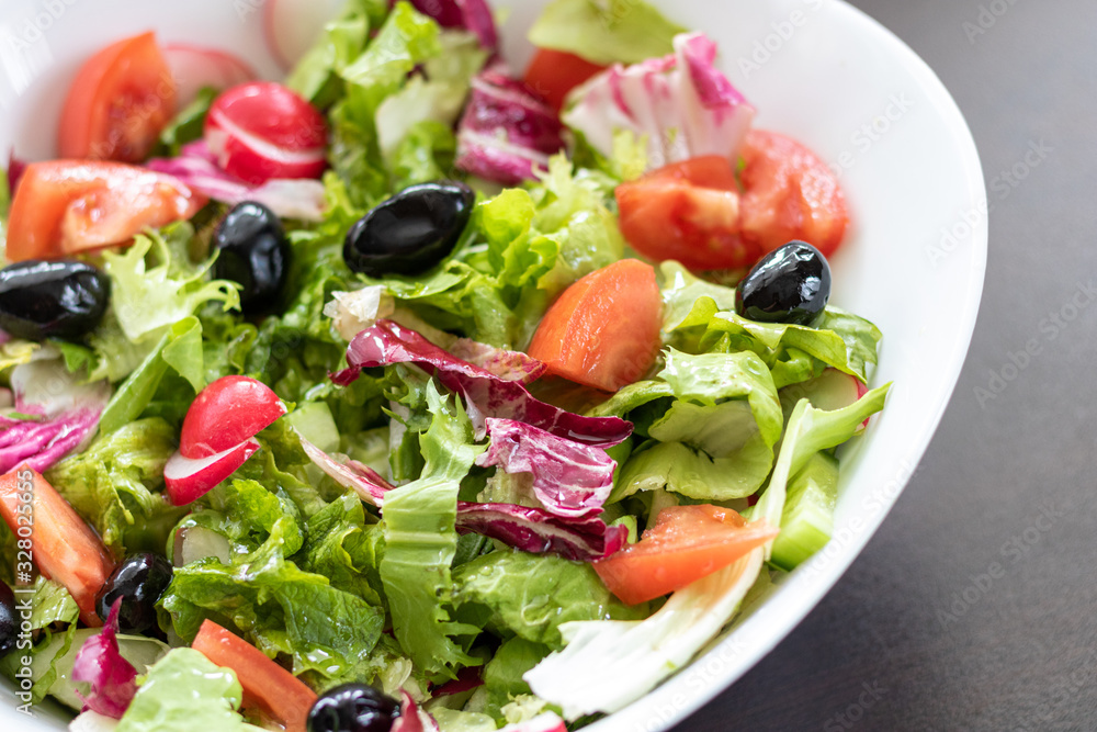 Green vegan salad from green leaves mix and vegetables in white bowl.Summer Easter diet salad dish of lettuce, radicchio, Lollo Rossa, endives, radishes, green onions, cucumbers, olives and tomatoes