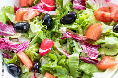 Green vegan salad from green leaves mix and vegetables in white bowl.Summer Easter diet salad dish of lettuce, radicchio, Lollo Rossa, endives, radishes, green onions, cucumbers, olives and tomatoes