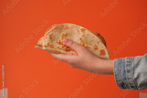 Mexican national food taco or Tatar national food kystyby in hand on an orange background.Food in a tortilla.National food concept photo