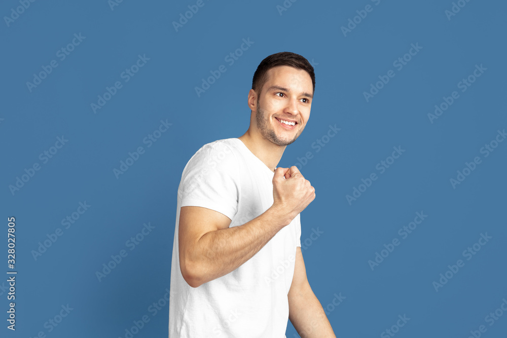 Fototapeta premium Winner, strong. Caucasian young man's portrait isolated on blue studio background. Beautiful male model in casual style, pastel colors. Concept of human emotions, facial expression, sales, ad.