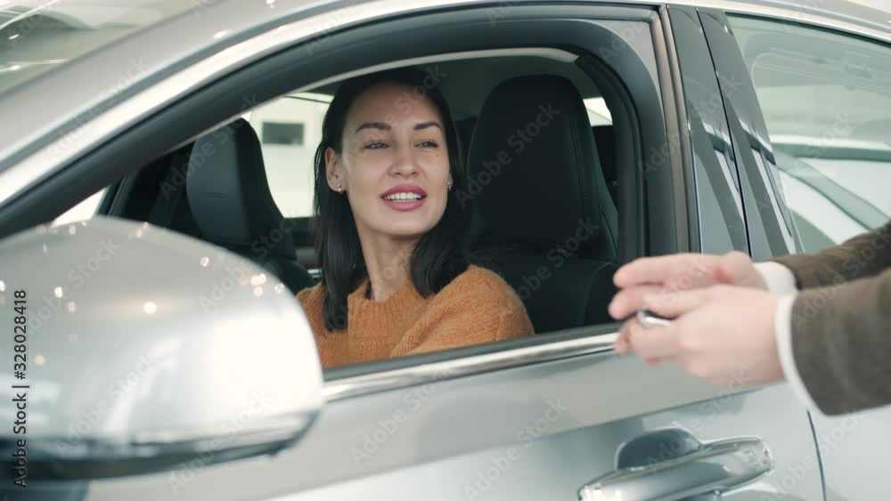 Happy young woman is getting key fob from salesman in automobile showroom buying car enjoying purchase. Business, deals and positive emotions concept. Happy young woman is getting key fob from salesman in automobile showroom buying car enjoying purchase. Business, deals and positive emotions concept.