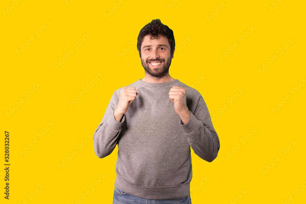 young handsome man feeling happy, positive and successful, celebrating victory, achievements or good luck over yellow background
