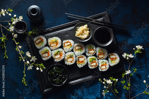 vegan sushi with tofu in General Tso sauce, avocado and fresh vegetables . on a table with branches of a blossoming tree