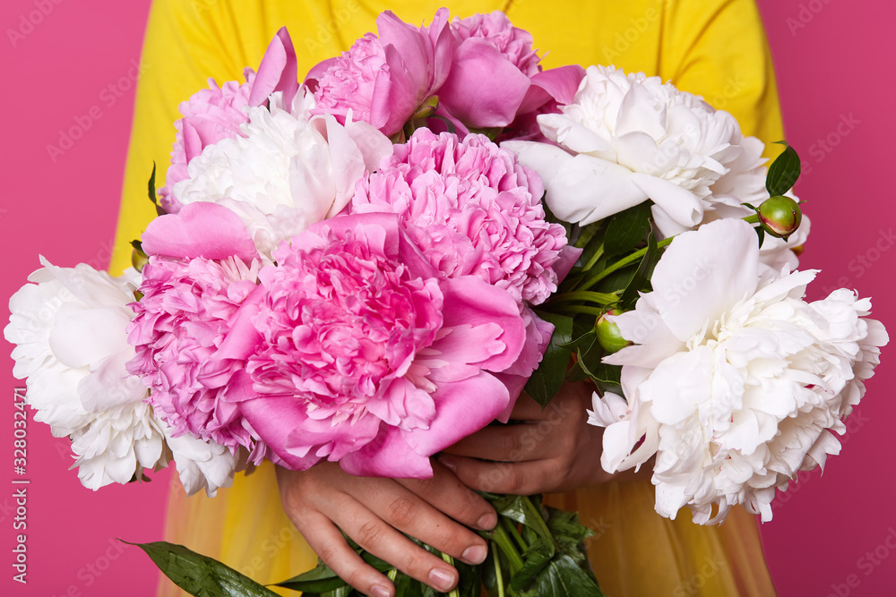 Φωτογραφία Studio shot of flowers bouquet of pinkand white peonies in hands of unknown woman wearing yellow outfit, faceless portrait of female with peony flowers isolated on rosy background