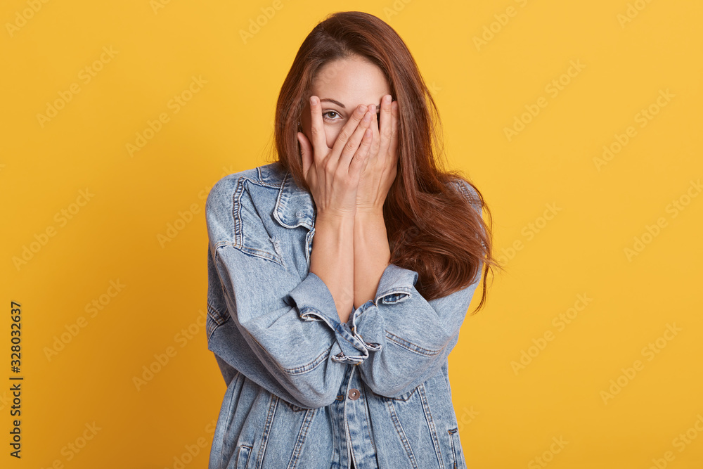 Φωτογραφία Portrait of cheerful young woman dresses denim casual jacket, covering her face with palms, posing isolated on bright yellow orange background in studio, expresses happyness