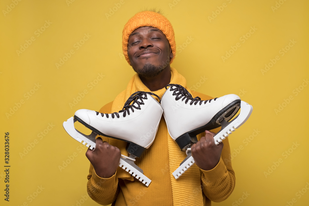 Φωτογραφία African guy in hat and scarf, holds skates in his hands smiling at camera