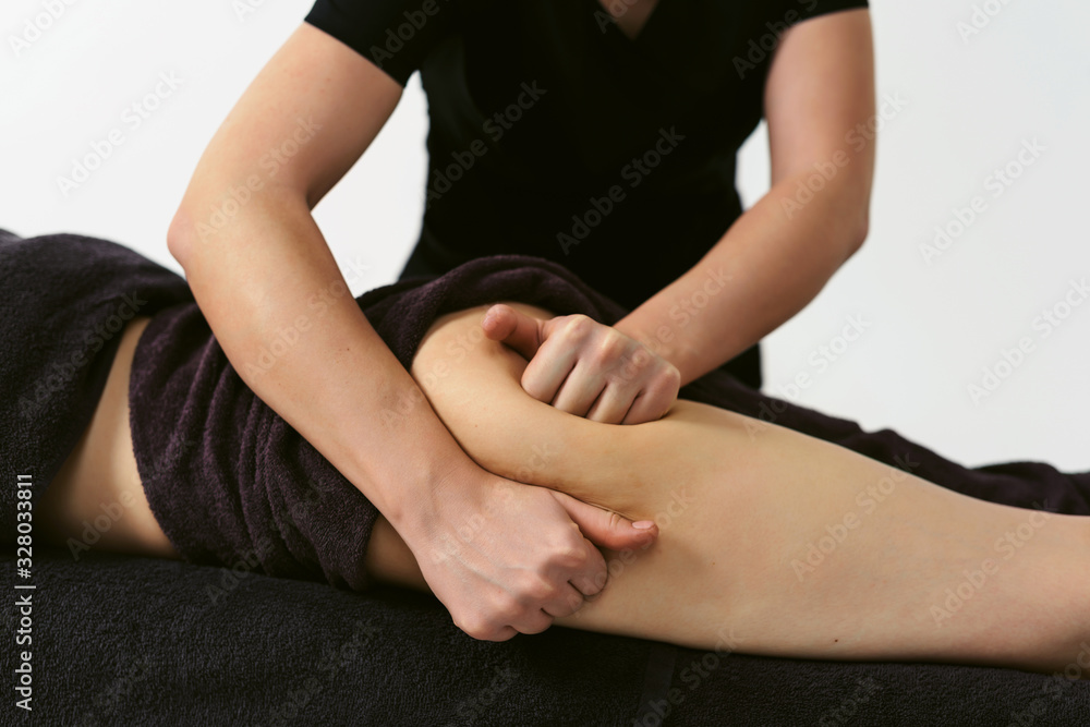 Fototapeta premium Anti cellulite legs massage for young woman in beauty salon. Wellness center spa fat burning for perfect skin. Healthy lifestyle. White background isolated