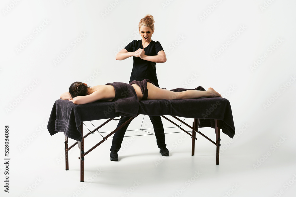 Funny fat burning massage. Portrait of cheerful woman masseur in uniforme near massage table with woman patient in wellness center. White background isolated Funny fat burning massage. Portrait of cheerful woman masseur in uniforme near massage table with woman patient in wellness center. White background isolated