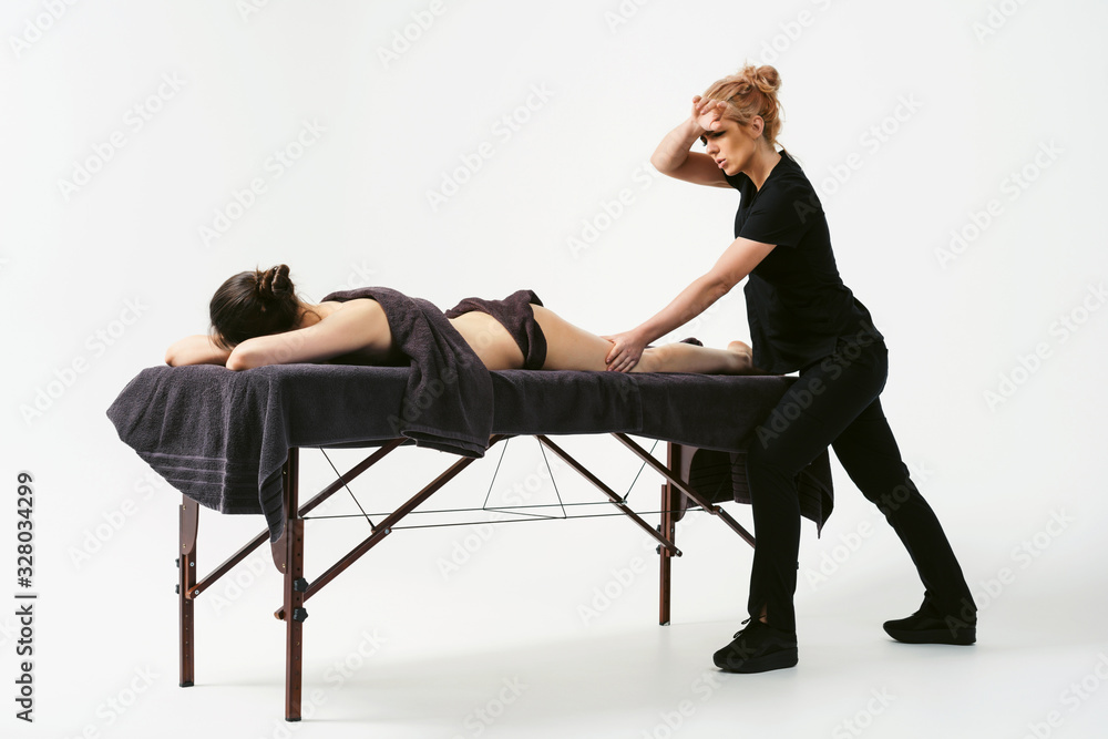 Funny fat burning massage. Portrait of cheerful woman masseur in uniforme near massage table with woman patient in wellness center. White background isolated Funny fat burning massage. Portrait of cheerful woman masseur in uniforme near massage table with woman patient in wellness center. White background isolated