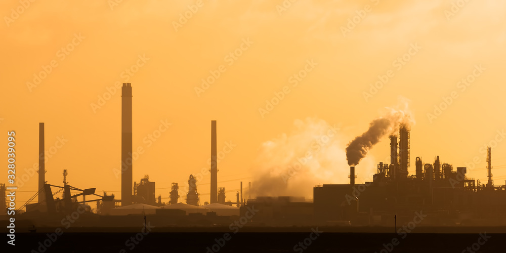 Dutch industrial plant with chimneys and windmill during sunset in Europoort, Rotterdam