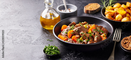 Beef meat and vegetables stew in black bowl with roasted baby potatoes. Dark background. Copy space.