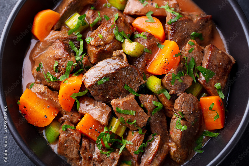 Beef meat and vegetables stew in black bowl. Dark background. Close up. - obrazy, fototapety, plakaty 