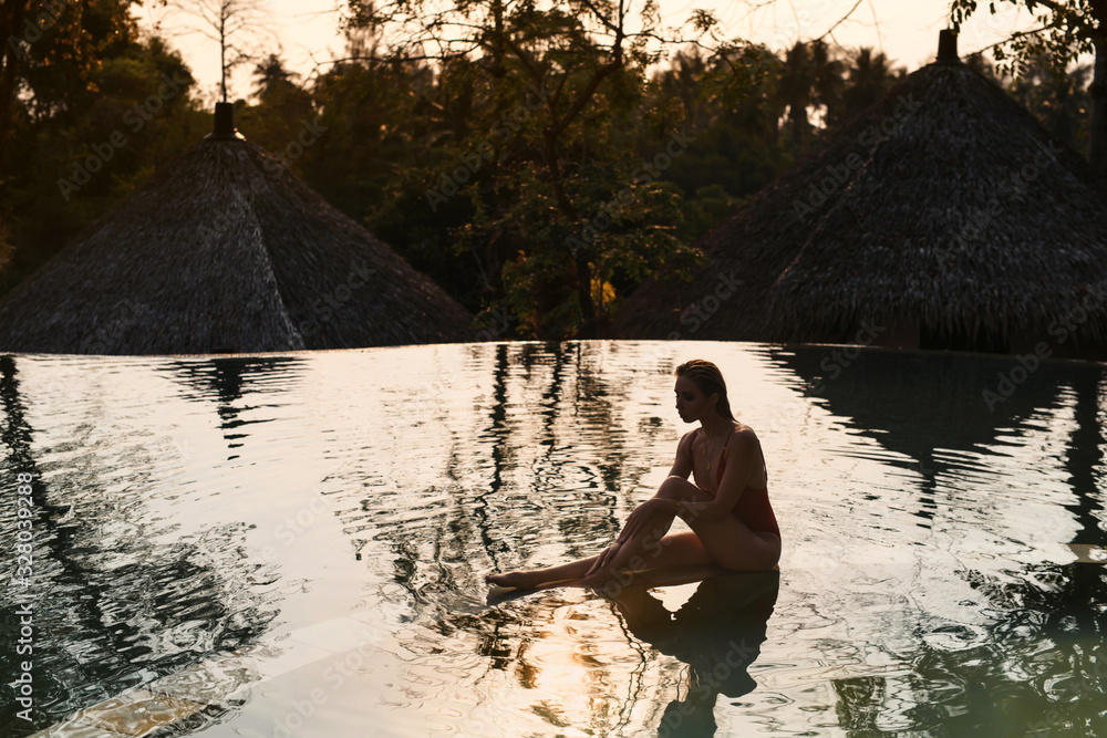 Φωτογραφία Young woman in orange swimsuit relaxing at sunset in the infinity pool with jung