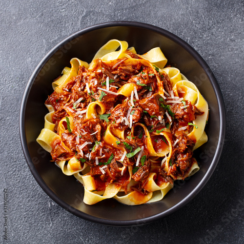 Pasta pappardelle with beef ragout sauce in black bowl. Grey background. Close up. Top view.