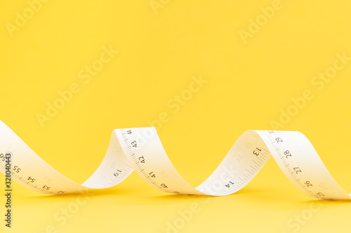 White paper measuring tape roll on solid yellow background with copy space using as nutrition diet, tailer designer or measure tool for furniture design