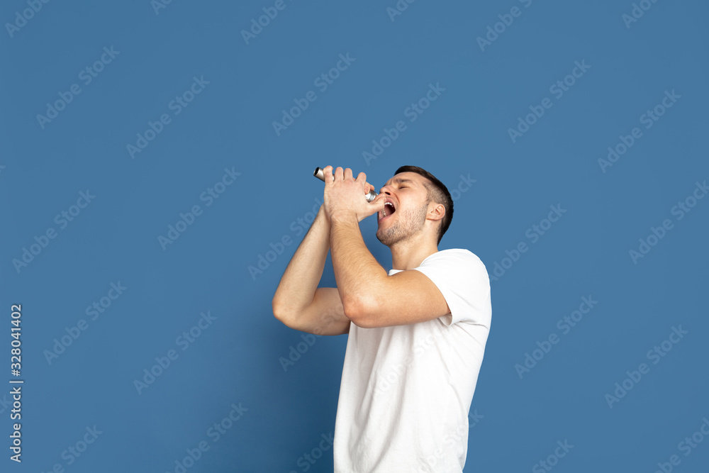Singing like celebrities, stars. Caucasian young man's portrait on blue studio background. Beautiful male model in casual style, pastel colors. Concept of human emotions, facial expression, sales, ad. Singing like celebrities, stars. Caucasian young man's portrait on blue studio background. Beautiful male model in casual style, pastel colors. Concept of human emotions, facial expression, sales, ad.