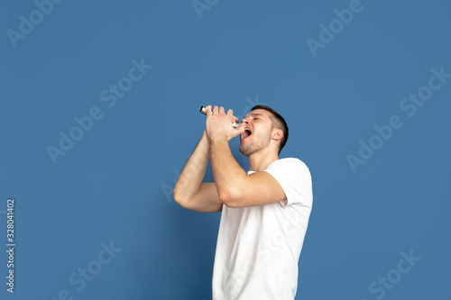 Singing like celebrities, stars. Caucasian young man's portrait on blue studio background. Beautiful male model in casual style, pastel colors. Concept of human emotions, facial expression, sales, ad.