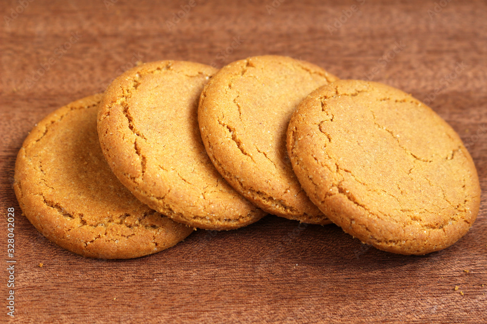 A row of four ginger biscuits on a dark wooden background A row of four ginger biscuits on a dark wooden background