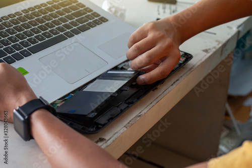 The technician is changing batteries to fix the laptop computer with Thai keyboard.