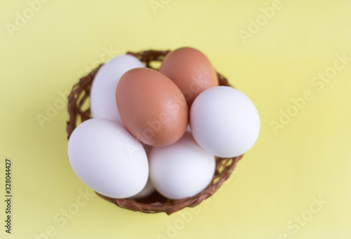 Top view of chicken eggs in an egg basket on yellow. Fresh chicken eggs with copy space. Natural healthy food concept White and one brown egg in a basket.