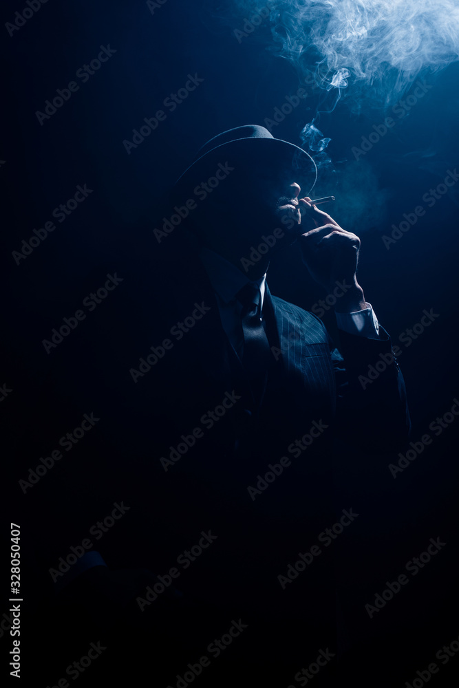 Silhouette of mafioso smoking cigarette on dark background