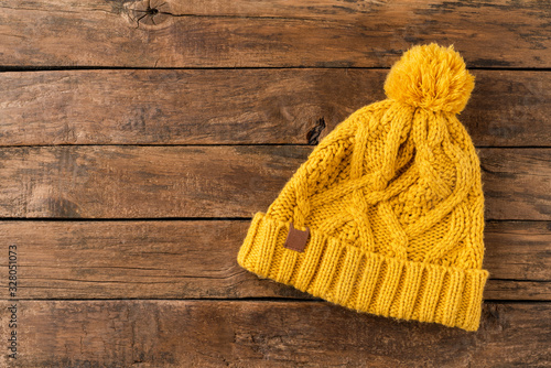 Yellow winter hat with pompon on wooden background with copyspace. Top view