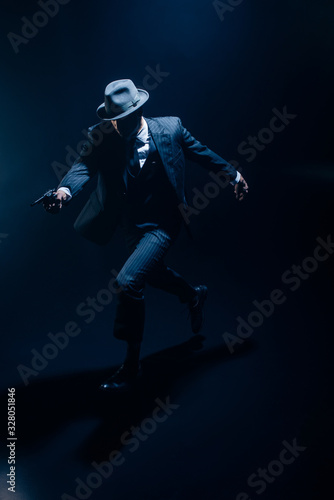 Gangster with outstretched hand aiming weapon and running on dark