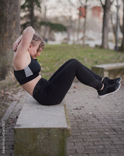 young blonde girl with blue eyes and sports black outfit doing outdoors exercises in a park on a warm winter afternoon