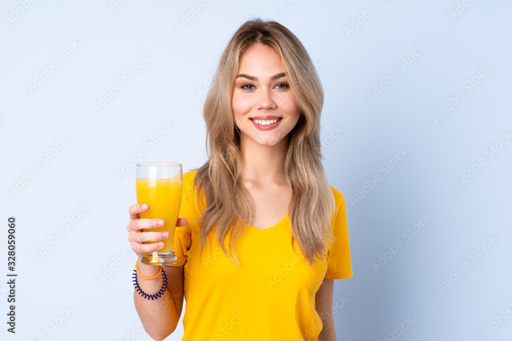 Teenager Russian girl holding an orange juice isolated on blue background smiling a lot Teenager Russian girl holding an orange juice isolated on blue background smiling a lot