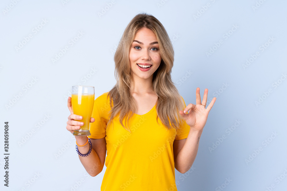 Teenager Russian girl holding an orange juice isolated on blue background showing ok sign with fingers Teenager Russian girl holding an orange juice isolated on blue background showing ok sign with fingers
