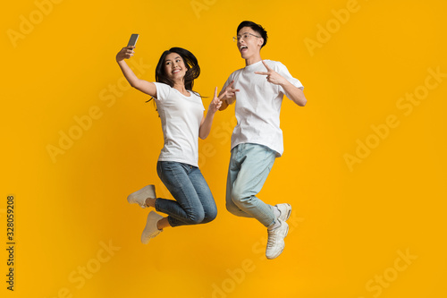 Crazy asian couple jumping and taking selfie on smartphone