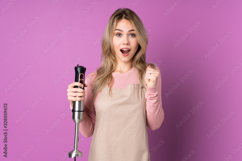 Teenager Russian girl using hand blender isolated on purple background celebrating a victory in winner position Teenager Russian girl using hand blender isolated on purple background celebrating a victory in winner position