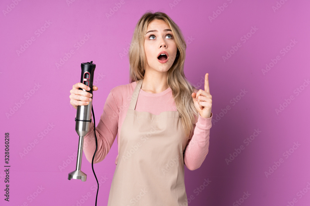 Teenager Russian girl using hand blender isolated on purple background surprised and pointing up Teenager Russian girl using hand blender isolated on purple background surprised and pointing up