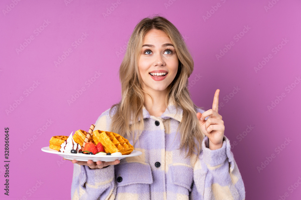 Teenager Russian girl holding waffles isolated on purple background pointing up a great idea Teenager Russian girl holding waffles isolated on purple background pointing up a great idea