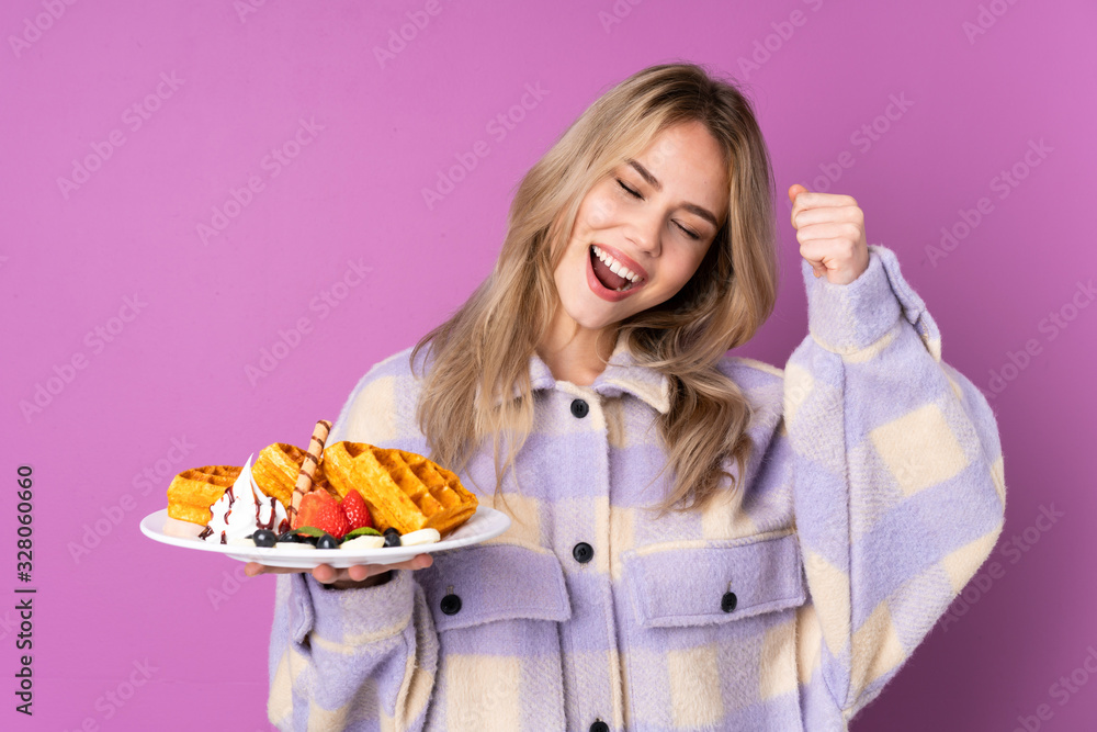 Teenager Russian girl holding waffles isolated on purple background celebrating a victory Teenager Russian girl holding waffles isolated on purple background celebrating a victory