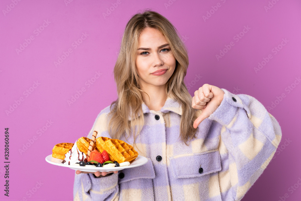 Teenager Russian girl holding waffles isolated on purple background showing thumb down Teenager Russian girl holding waffles isolated on purple background showing thumb down
