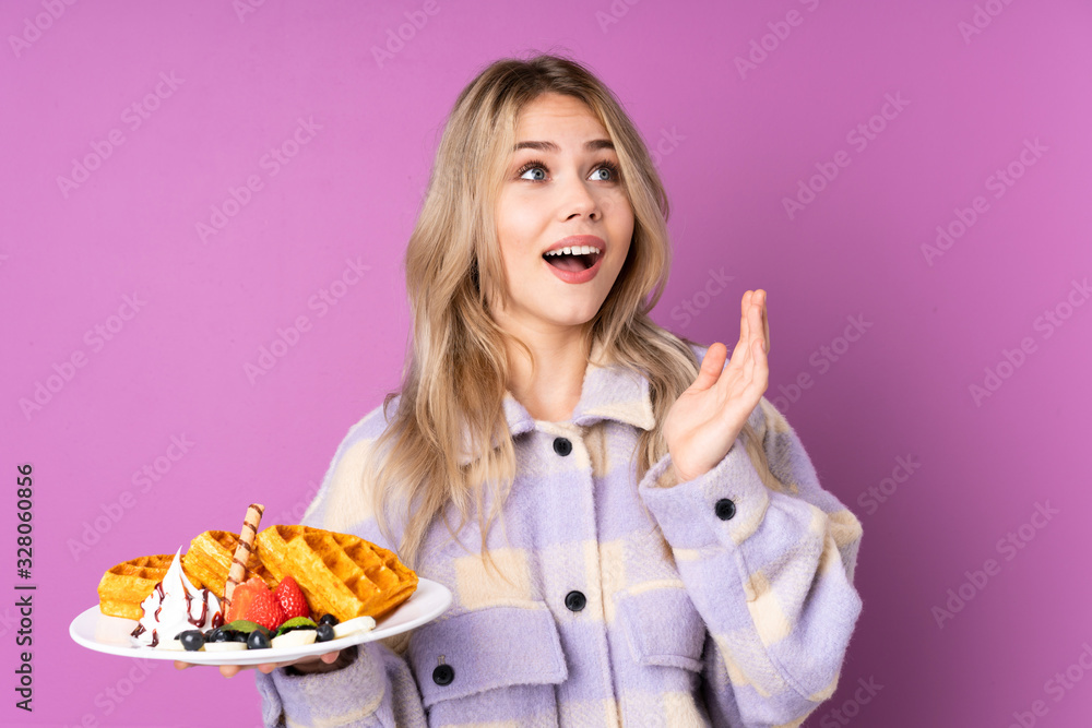 Teenager Russian girl holding waffles isolated on purple background with surprise facial expression Teenager Russian girl holding waffles isolated on purple background with surprise facial expression