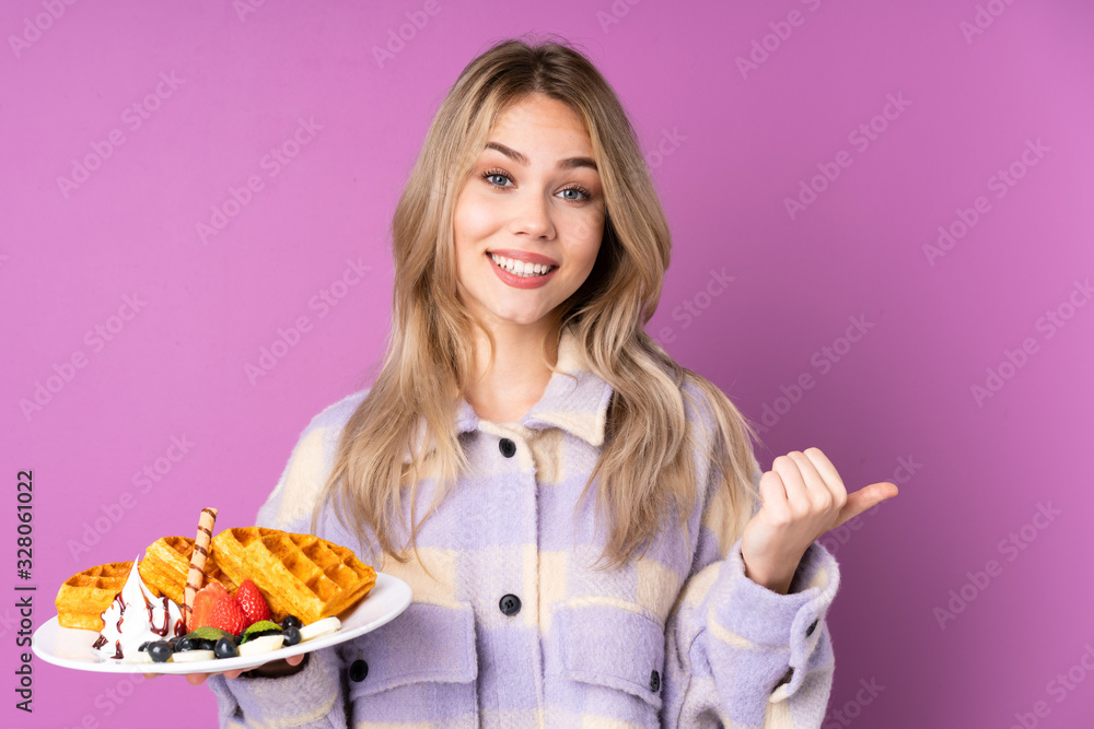 Teenager Russian girl holding waffles isolated on purple background pointing to the side to present a product Teenager Russian girl holding waffles isolated on purple background pointing to the side to present a product