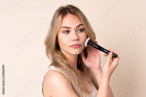 Teenager blonde girl with makeup brush over isolated background