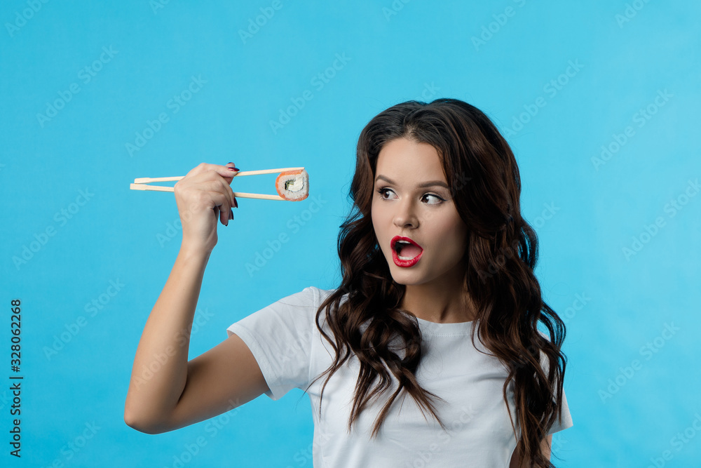 Obraz premium The beautiful brunette girl opened her mouth in surprise. Girl shows emotions she holds hashi with wooden chopsticks sushi. Lady with a cool haircut. The concept of beauty, fashion, advertising.