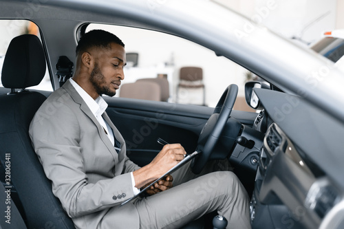 Man Taking Notes Sitting In Driver's Seat In Automobile Dealership © Prostock-studio