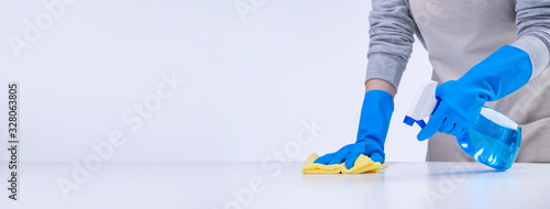 Εκτύπωση καμβά Young woman housekeeper is doing cleaning white table in apron with blue gloves, spray cleaner, wet yellow rag, close up, copy space, blank design concept