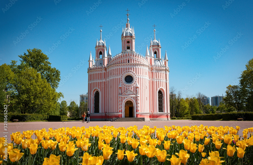 Orthodox Church in pink against the blue sky  in front of a flowerbed with yellow tulips