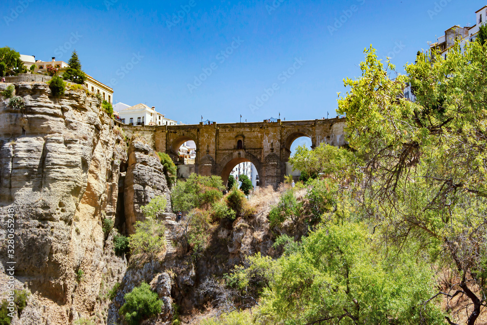 Stone medieval bridge in the city of Ronda Spain view from the side, view on the rocks and gazebo on the cliffs,  famous tourist site