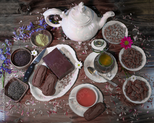 Tea table with vintage mother-of-pearl tea pot, cups and  saucers, flowers, pecans, cashews, almonds, dark chocolate and chocolate biscotti snacks. A variety of loose teas are available for brewing. 