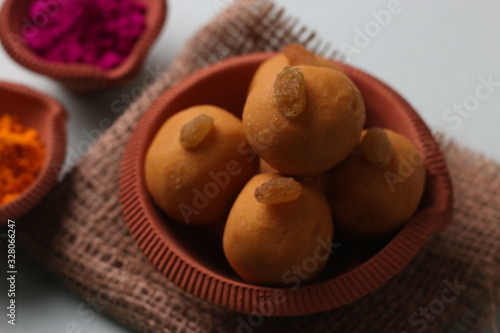 Popular Indian Sweet Besan Laddoo gram flour sweet balls and Gujia or Karanji arepopular Holi snacks served in earthen bowls.