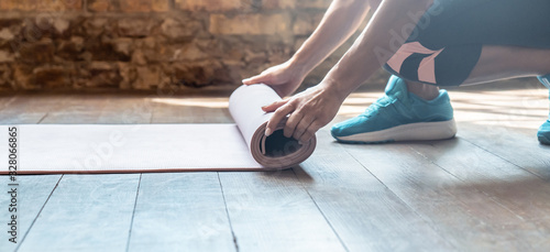 Closeup hand active sporty woman rolling unrolling fold back beige sport foam rubber mat keep fit do exercise before practice yoga training work modern gym fitness studio healthy lifestyle concept. © insta_photos