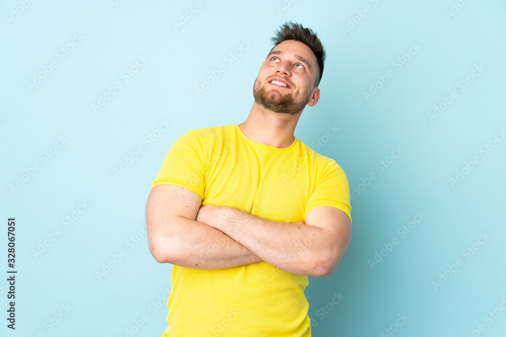 Russian handsome man isolated on blue background looking up while smiling